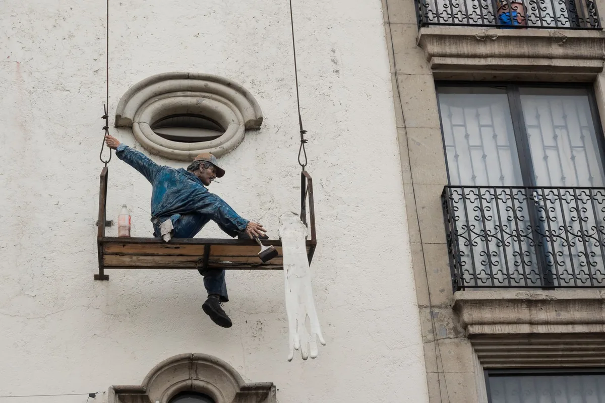 Operario aplicando tratamiento protector sobre la fachada de un edificio desde una plataforma colgada, una fase clave para proteger el muro del salitre